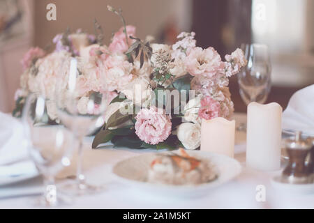 Blumenstrauß auf dem Tisch. Weingläser im Vordergrund. Hochzeit oder Gala Dinner. Die Tische und Stühle für Gäste, serviert mit Besteck und Crocker Stockfoto