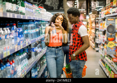Afrikanische Paar Einkaufen in trinken Abschnitt im Supermarkt. Paar Einkaufen am Markt beim Kaufen kaltes Getränk. Hübscher Kerl holding Shopping Stockfoto
