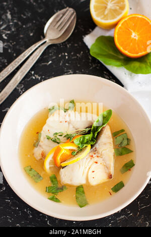 Gebratener Kabeljau mit Citrus Butter in einer Schüssel auf schwarz Tabelle Stockfoto