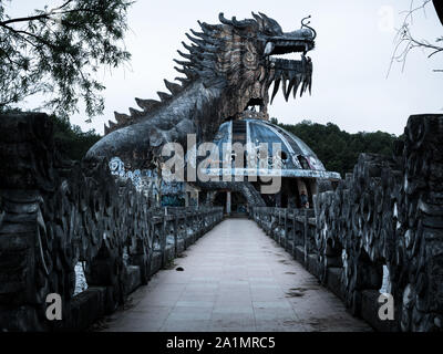 Riesig und unheimlich stone Dragon mit Spikes und offener Mund mit Zähnen in der Seitenansicht mit Fußweg an verlassenen Water Park, Thuy Tien See, Hue, Vietnam Stockfoto