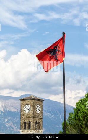 Der Uhrturm und Abanian Flagge auf gjirokastra Festung Schloss mit Berge und blauer Himmel mit weißen Wolken im Hintergrund. Selektive konzentrieren. Stockfoto