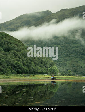 Vertikale Landschaft. Loch Duich, in der Nähe von Kintail, in den Highlands von Schottland, mit Fischerboot auf dem Ufer, niedrige Wolken um die Berge hängen Stockfoto