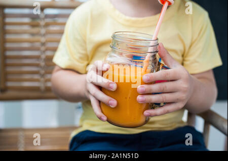 Junge trinkt Smoothie Papaya. Gesunde Ernährung Konzept. Schwarzes Holzbrett mit Platz für Text Stockfoto