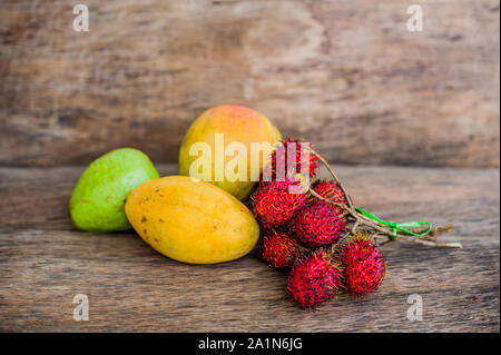 Tropische Früchte auf dem alten Holzhintergrund. Rambutan, Banane, Mango, Guava. Stockfoto