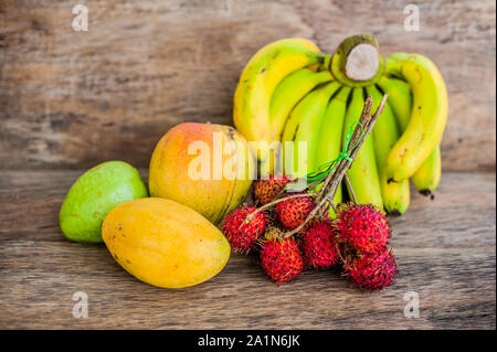 Tropische Früchte auf dem alten Holzhintergrund. Rambutan, Banane, Mango, Guava. Stockfoto