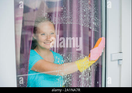 Schöne weibliche Magd die Hausarbeit, während mit einem Spray, Waschen von Fenstern Stockfoto