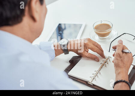 Hände von den alten Mann an den Tisch, ein Mann mit einem Stift schreiben in einem Notebook. Stockfoto