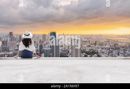 Frau in weißen Hut sitzen auf Gebäude, Terrasse, Blick auf die Stadt bei Sonnenuntergang Stockfoto