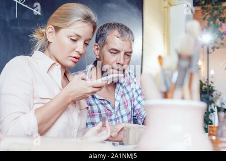 Glücklich verheiratetes Paar am Tisch sitzen in der Töpferei. Frau macht Foto auf dem Smartphone. Stockfoto