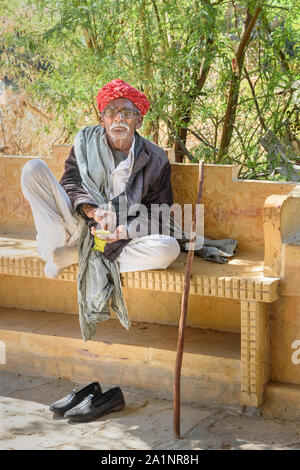 Jaisalmer, Indien - Februar 16, 2019: Ältere indische Mann mit grauen Schnurrbart trägt rote Rajasthani turban oder pagari auf der Bank in Jaisalmer. Rajastha Stockfoto