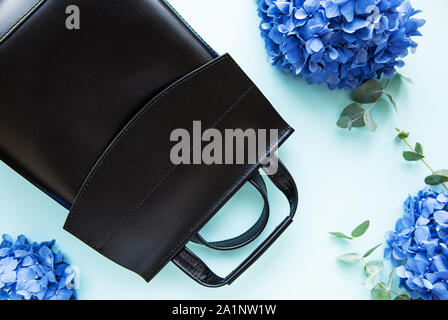 Schwarz Leder Rucksack mit Blaue Hortensie Blumen auf einem hellblauen Hintergrund. Stockfoto