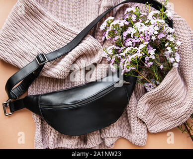 Flach Zusammensetzung des schwarzen Hüfttasche, Pullover und Blumen auf braunem Hintergrund Stockfoto