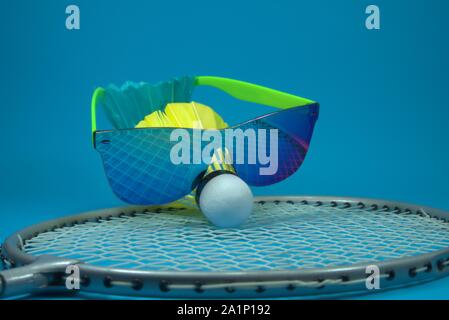 Bunt gefiederten Badminton Federball mit Sonnenbrille ruht auf einem Schläger auf einem blauen Hintergrund in der Nähe zu Still Life Stockfoto