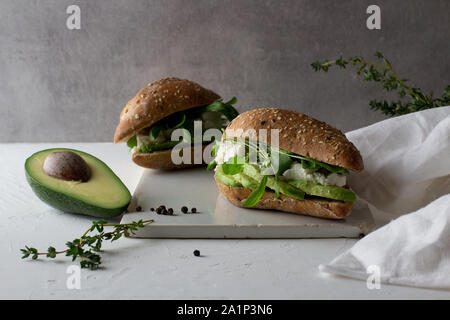 Zwei Sandwiches von Vollkorn Glutenfreie hausgemachtes Brot mit Avocado und Ricotta auf Weiß rustikal Keramik Schneidbrett. Gesunde hausgemachte Stockfoto