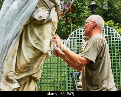 Ettal, Deutschland, August 6., 2019: Mann mittleren Alters, ein Restaurator oder Bildhauer, stellt ein Sandstein Abbildung im Garten und Park von Schloss Linderhof. Stockfoto