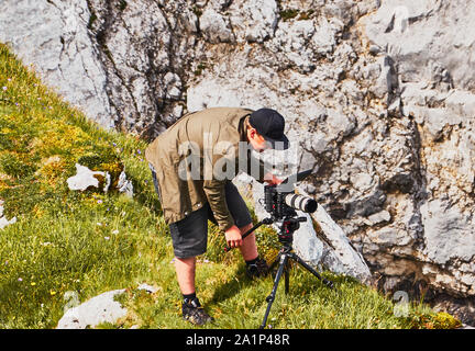 Garmisch-Partenkirchen, August 8., 2019: mich Fotograf professionelle Videokamera auf einem Stativ neben einem Kalkstein bei der Arbeit Stockfoto