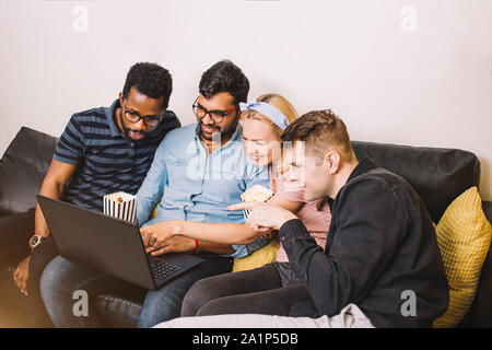Gruppe von Freunden genießt die Zeit zusammen und suchen am Laptop. Multirassischen junge Menschen im Wohnzimmer zu Hause sitzen, Videos, po Essen Stockfoto