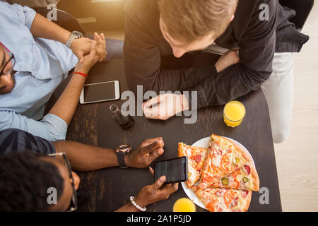 Blick von oben auf die Gruppe von Freunden am Tisch sitzen im Cafe, Mittagessen, essen Pizza, Saft trinken, über Handy, schreiben Sie soziale Netzwer Stockfoto