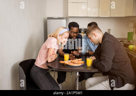 Aufnahme von Studenten am Tisch in Hostel Küche sitzt und auf dem Bildschirm des Mobiltelefons zusammen suchen. Freunde etwas aufpassen auf Smartphone, während Hav Stockfoto