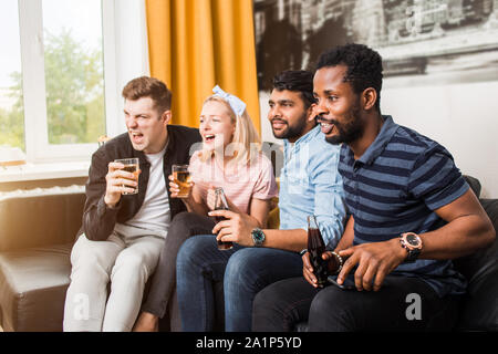 Freundschaft, Freizeit, Erholung, Home Party Konzept. Freunde Fernsehen zu Hause und trinken Bier sitzen auf der Couch im Wohnzimmer. Sport und Unterhaltung Stockfoto