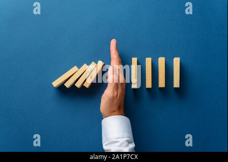 Blick von oben der männlichen Hand störende zusammenbrechenden Dominos in einem konzeptionellen Bild der Krisenbewältigung. Über Marine blauen Hintergrund. Stockfoto