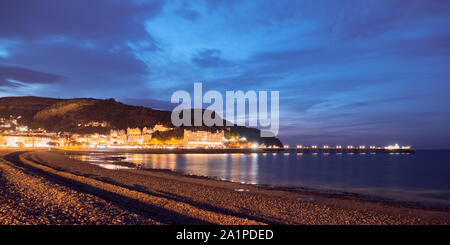Am Abend Blick auf die beleuchteten Ufer und Pier von Llandudno Wales, mit Dürren, Wolken und Licht reflektierenden Meer Stockfoto