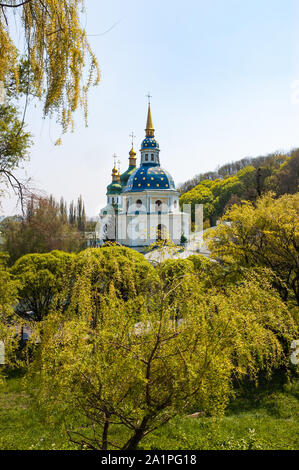 Ein Blick auf die Vydubitsky Kloster mit goldenen und blauen Dächern mit gelben Sternen in der Mitte des Waldes im Botanischen Garten von Kiew, Ukraine Stockfoto