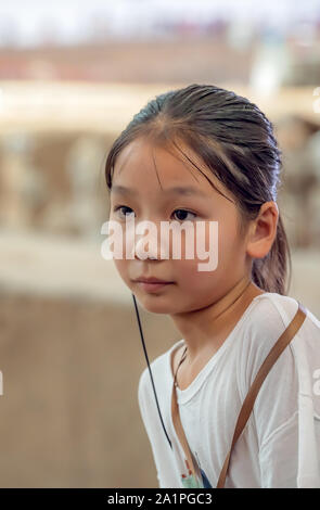 Xian, China - Juli 2019: Kleine chinesische Mädchen mit einem abhörgerät in ihr Ohr, der ihr erlaubt zu hören Führer zur Tour, während ein Besuch im Museum, Sh Stockfoto