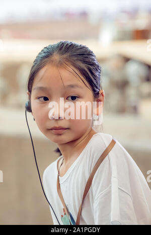 Xian, China - Juli 2019: Kleine chinesische Mädchen mit einem abhörgerät in ihr Ohr, der ihr erlaubt zu hören Führer zur Tour, während ein Besuch im Museum, Sh Stockfoto