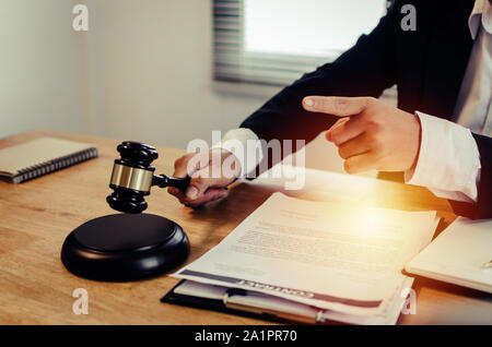 Justiz Rechtsanwalt in schwarzen Anzug Zeigefinger und klopfen Holz- richter Hammer mit Dokument auf Arbeitsplatz Schreibtisch im Gerichtssaal Büro Stockfoto