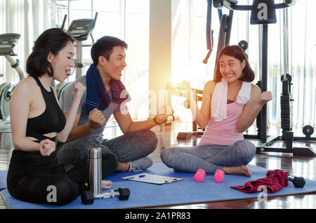 Gruppe junge sportliche Leute aufheitern und zusammen lachen sitzen auf Yoga Matte in Fitness Gym nach Training übung am Morgen Stockfoto
