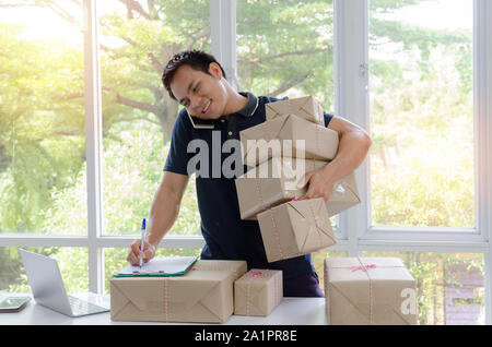 Kmu. gutaussehenden jungen asiatischen Delivery Man glücklich nach neuen Auftrag vom Kunden und heben viele Verpackung Paket mit Handy im Home Office Stockfoto