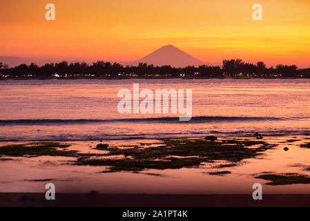 Gili Trawangan als im Hintergrund, Bali, Indonesien von Gili Meno mit Mount Agung nach Sonnenuntergang gesehen. Stockfoto