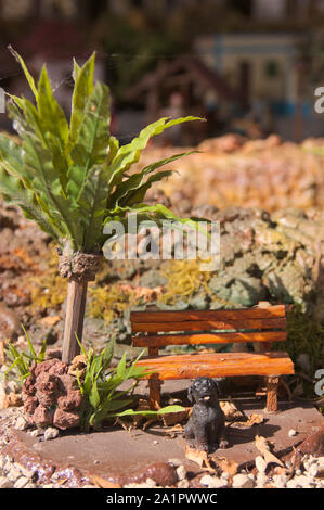 Kleine Figuren, die für einen Hund neben einer Bank und eine Palme in einer kleinen Stadt park Stockfoto