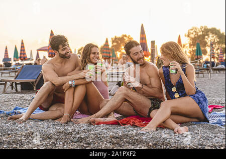 Zwei junge Paare Entspannung trinken Bier am Strand in einem Sommer Sonnenuntergang. Junge Menschen lifestyle Konzept Stockfoto