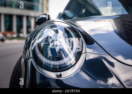 Russland Moskau 2019-06-17 Closeup Scheinwerfer des neuen glänzenden Luxus dunkelblau Sportwagen Porsche 911 auf der Straße geparkt, vorne unten, Sky reflecti Stockfoto