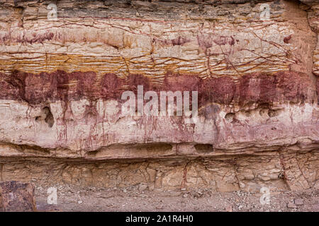 Eine Klippe in der makhtesh Ramon in Israel zeigen verschiedene Schichten von Gesteinen und Böden, darunter eine rote Schicht, Blutungen in der Ebene darunter Stockfoto