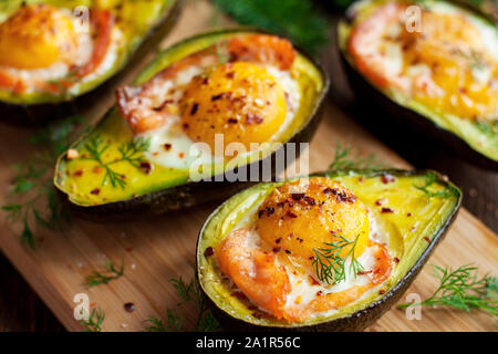 Gebackene Eier in Avocado mit Räucherlachs auf Holz Schneidebrett. Gesunde Mahlzeit Stockfoto