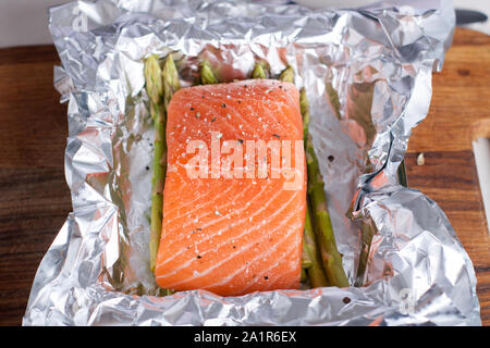 Lachs mit Salz und Pfeffer gewürzt mit Spargel in Folie. Zubereitung von Lachs in Folie gebacken mit Pesto, Tomaten und Spargel Stockfoto