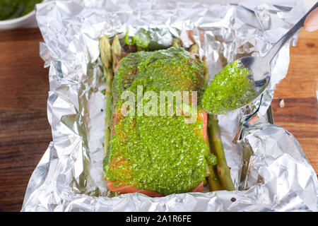 Lachsfilet mit Pesto. Zubereitung von Lachs in Folie gebacken mit Pesto, Tomaten und Spargel Stockfoto