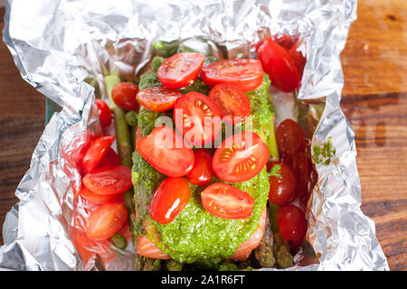 Roher Lachs, Spargel, Pesto, Tomaten. Zubereitung von Lachs in Folie gebacken mit Pesto, Tomaten und Spargel Stockfoto