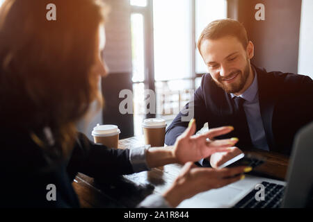Junge Frau mit Mobiltelefon in den Händen, eine appontment mit Kollegen zu machen, während ihr Kollege pensice nach unten schauen. Stockfoto