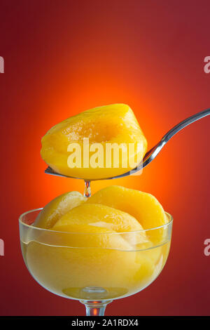 Tasse und Löffel mit Pfirsichen in Sirup mit orangefarbenen Hintergrund. Stockfoto