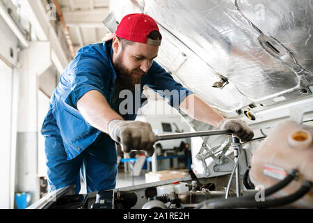 Junge Techniker in Arbeitskleidung biegen über Motor des Pkw oder Lkw bei der Prüfung oder für die Behebung von kleinen Details Stockfoto