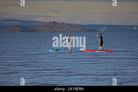 Portobello, Edinburgh, Schottland, Großbritannien. September 2019. Zwei Mädchen auf Stand Up Paddle Boards genießen 15 Grad und Sonnenschein auf dem Firth of Forth mit Inchkeith Island im Hintergrund. Stockfoto