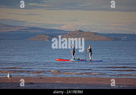 Portobello, Edinburgh, Schottland, Großbritannien. September 2019. Zwei Mädchen auf Stand Up Paddle Boards genießen 15 Grad und Sonnenschein auf dem Firth of Forth mit Inchkeith Island im Hintergrund. Stockfoto