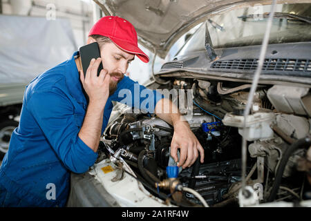 Junge zuversichtlich Master der technischen Service über Smartphone, während der Beratung eines Kunden und Prüfung der Motor der Maschine Stockfoto