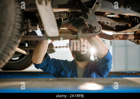 Schwere männliche technischer Ingenieur von Auto Reparatur Service Suche bei einem von Details beim Stehen unter der Maschine Stockfoto