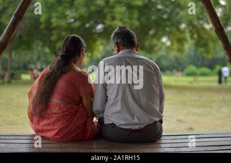 Senioren indische Paar liest aus mobile Schuß von hinten, während sie in einem Park in Neu Delhi sitzen Stockfoto