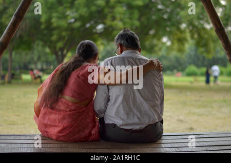 Senioren indische Frau liest aus Mobile und mit der Hand über die Schulter geschossen Ihres Mannes von hinten, während sie in einem Park in Neu Delhi sitzen Stockfoto